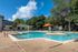 Inviting outdoor pool with fountains and a shaded seating area, surrounded by lush greenery in a serene apartment community.