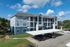 Modern three-story apartment complex with spacious balconies and covered parking, set against a vibrant blue sky and lush greenery.