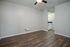 Modern apartment room with stylish wood flooring, neutral gray walls, and a ceiling fan, leading to a cozy kitchenette with white cabinetry.
