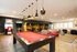 Vibrant recreational room featuring a modern red pool table, cozy lounge seating, arcade games, and sleek pendant lighting.