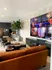 Modern living room with leather sofa, wall-mounted TV, and sleek decor; open-concept kitchen with stylish cabinetry in the background.