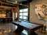 Chic apartment game room featuring a sleek pool table, industrial-style kitchen bar with modern seating, and eye-catching wall art under stylish lighting.