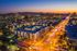 Stunning aerial view of a vibrant cityscape at dusk, featuring modern apartment complexes illuminated by streetlights and surrounded by distant mountains.