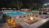 Luxurious outdoor area featuring a sparkling pool, stylish fire pit lounge, and elegantly lit seating, perfect for evening relaxation.