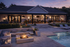 Charming patio area at dusk featuring a cozy fire pit, luxurious seating, and a sparkling pool adjacent to a beautiful modern home.