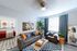 Chic living room with a modern gray sofa, vibrant accent cushions, and stylish artwork, featuring a sunlit window and lush green plant for a cozy ambiance.