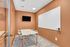 Modern conference room with sleek orange walls, a spacious table, four chairs, flat-screen TV, and a large whiteboard for dynamic presentations.