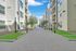 Charming modern apartment complex with spacious walkways, lush greenery, and elegant architecture under a clear blue sky.