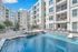 Luxurious apartment complex featuring a sparkling blue swimming pool, surrounded by modern multi-story buildings and inviting lounge chairs under a sunny sky.
