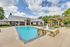 Inviting community pool area with a charming brick clubhouse, sun loungers, and pergola, perfect for relaxation and gatherings.