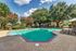 Inviting outdoor pool area surrounded by lush greenery and blooming trees, featuring comfortable lounge chairs for relaxation under a sunny sky.