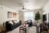 Chic living room boasting a modern black sofa, stylish accent chair, and elegant floor lamp. Natural light pours in through large windows, enhancing the cozy ambiance. Contemporary art adorns the walls, adding a touch of sophistication.