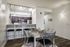 Modern dining area with elegant decor, featuring a sleek table set for four, high stools at a breakfast bar, and contemporary lighting in a stylish open-concept kitchen.
