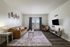 Bright and inviting living room with modern decor, featuring a cozy leather sofa, elegant armchair, mounted TV, and stylish coffee table. Large windows with curtains allow for ample natural light.