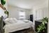 Charming bedroom with a cozy bed, elegant white linens, and vibrant green plants enhancing a modern, bright ambiance.