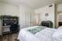 Bright, stylish bedroom with white bedding, a compact workspace adorned with plants, and a glimpse of an elegant bathroom.