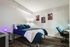 Modern bedroom with sleek design featuring a cozy bed with navy bedding, ambient lighting, and space-themed wall art, creating a serene and stylish retreat.