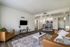 Bright and inviting living room with stylish decor, featuring a cozy sofa, wall-mounted TV, and open access to a modern kitchen and dining area.