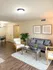 Cozy living area featuring a stylish gray sofa, elegant armchairs, and a beautiful coffee table with plant decor. Bright, airy space with wooden flooring and wall art, perfect for relaxing and entertaining.