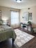 Charming bedroom with elegant decor, featuring a floral bedding set, cozy reading nook, and natural light filtering through sheer curtains.