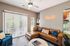 Chic living room with stylish leather sectional, cozy throw pillows, vibrant wall art, and a trendy neon sign, complemented by large windows and modern decor.