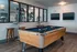 Modern recreation room with billiards table, stylish bar stools, and gym view, perfect for entertainment and fitness.