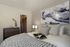 Chic bedroom featuring cozy bed with textured throw, abstract wall art, elegant lighting, and a spacious walk-in closet in the background.