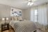 Cozy bedroom featuring soft lighting, elegant abstract art, and a plush knit blanket on a comfortable bed next to a sunlit window with flowing curtains.