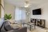 Bright and inviting living room with a cozy gray sofa, modern coffee table, elegant floor lamp, and large wall-mounted TV, complemented by lush greenery and stylish decor.