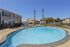 Inviting apartment complex showcasing a sparkling outdoor pool with lounge chairs and umbrellas, framed by lush landscaping and elegant two-story buildings.