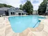 Inviting apartment complex pool area with sparkling water, modern clubhouse, and lush green surrounds.