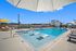 Luxurious rooftop pool with sun loungers and umbrellas, offering breathtaking city views against a clear blue sky.