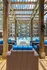 Luxurious outdoor pool area with modern wicker furniture and vibrant blue cushions, framed by elegant wooden pergolas, set against a stylish apartment building backdrop.