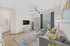 Modern living room featuring a cozy gray sofa, stylish armchairs, and a flat-screen TV. The space is enhanced by natural light through large windows, elegant decor, and contemporary flooring.