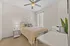 Bright bedroom with modern decor, stylish ceiling fan, and cozy bedding, featuring natural light from large window.