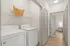 Bright and modern laundry area with washer, dryer, and ample storage, leading to a cozy room with elegant wood flooring.