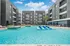 Modern apartment complex featuring a stunning outdoor pool with lounge seating, surrounded by sleek multi-story buildings under a bright blue sky.