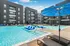 Luxurious apartment complex with a sparkling pool, modern lounge chairs, and elegant balconies under a clear blue sky.