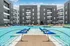 Modern apartment complex showcasing a stunning central pool area with sunbeds and umbrellas, surrounded by sleek multi-story buildings.