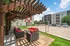Chic outdoor lounge with red-cushioned seating under a pergola, adjacent to a sand volleyball court and modern apartment complex.