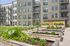 Modern apartment building with sleek balconies overlooking lush community gardens and charming landscaped paths.