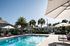 Inviting outdoor swimming pool area with sun loungers and umbrellas, surrounded by lush palm trees and well-maintained landscaping.