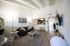 Modern living room with high ceilings, stylish gray sofa, chic artwork, and a cozy open-plan kitchen featuring a sleek breakfast bar.