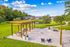 Picturesque outdoor area with pergola, seating, and lush greenery overlooking a serene pond.