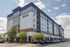 Modern apartment complex with vibrant facade and ample parking, showcasing convenient retail spaces on the ground floor and a mix of balconies under a clear blue sky.