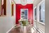 Bright dining area with a modern chandelier, colorful red accent wall, large windows, and green chairs around a sleek table.