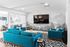 Modern living room with vibrant turquoise sofas, geometric black and white rug, and large wall-mounted TV, creating a stylish and inviting atmosphere.