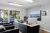 Modern office space with sleek black furniture, large windows offering natural light, and a scenic cityscape painting enhancing the ambiance.