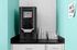 Modern coffee machine setup on a sleek black countertop with neatly arranged cups and an inviting teal wall.