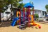 Vibrant playground set with slides and climbing areas surrounded by lush green trees and apartment buildings.
